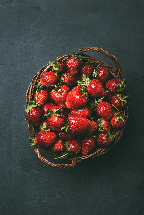 top view of fresh ripe sweet strawberries in wicker basket on black