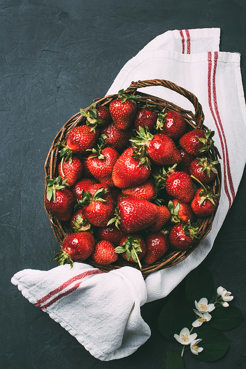 top view of fresh ripe sweet strawberries in wicker basket and towel on black