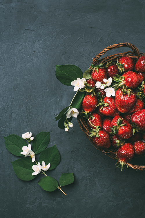 top view of beautiful jasmine flowers and fresh ripe strawberries in basket on black