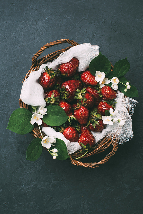 top view of fresh ripe strawberries and beautiful jasmine flowers in basket on black