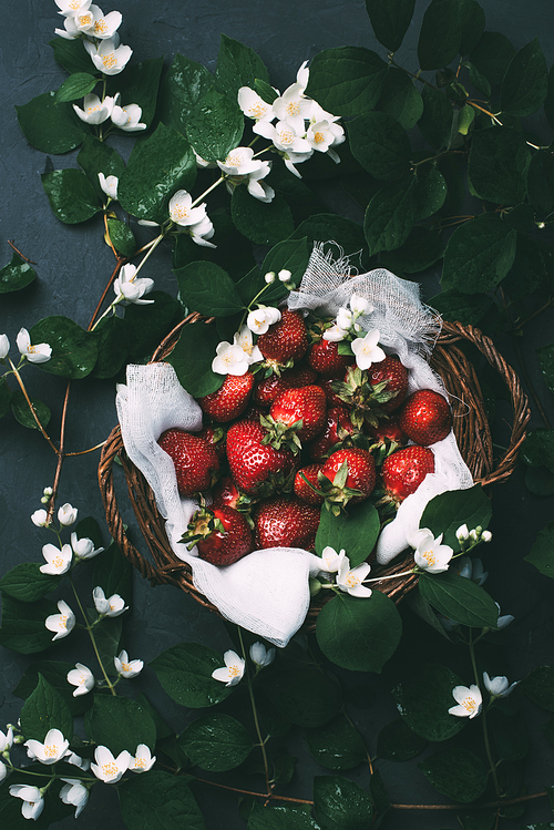 top view of beautiful jasmine flowers and sweet ripe strawberries in basket