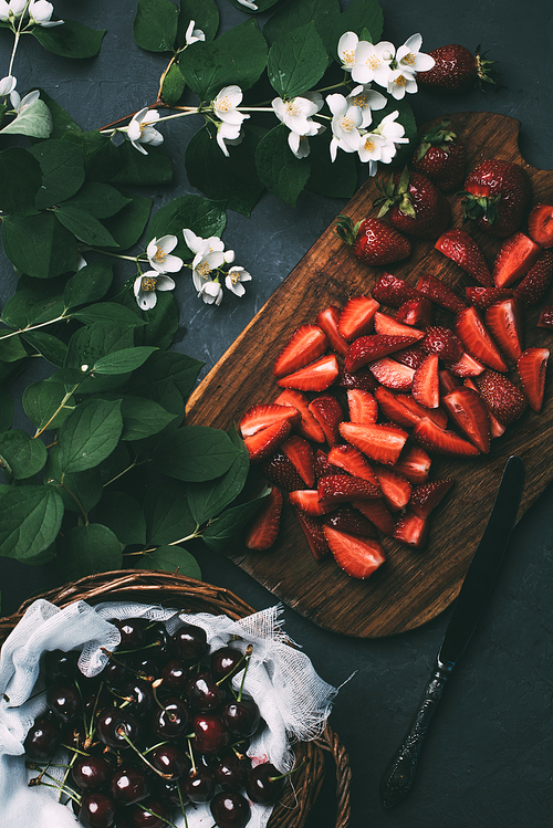 top view of beautiful jasmine flowers, sliced strawberries and ripe sweet cherries on black