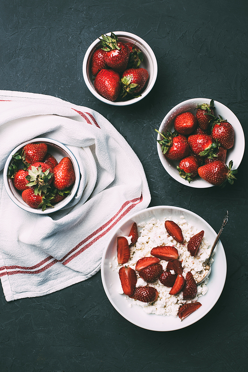top view of tasty healthy cottage cheese and fresh ripe strawberries in bowls on black