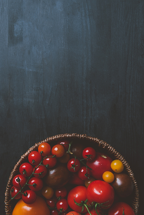 top view of red cherry tomatoes in wicker bowl on wooden background with copy space