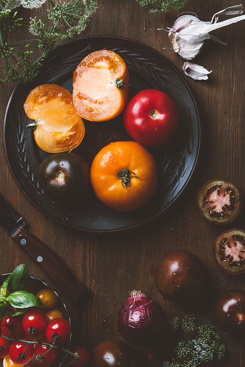 top view of different tomatoes on ceramic plate with knife on wooden background