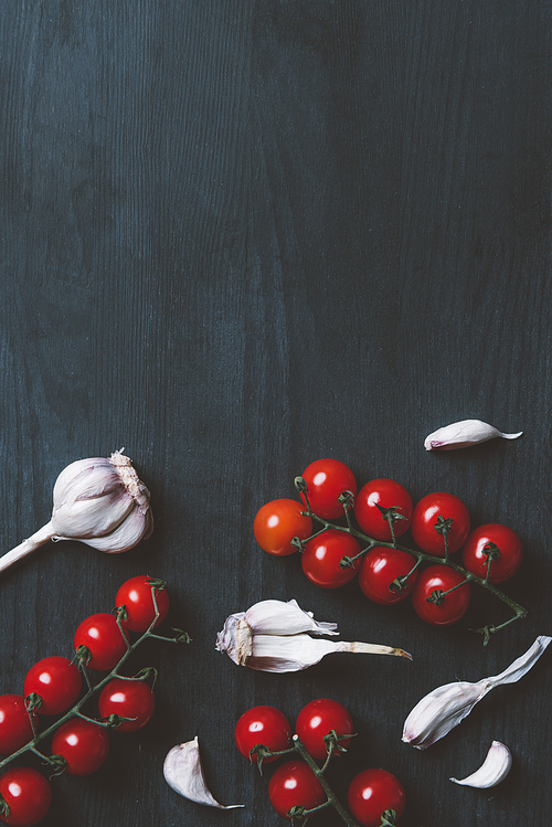 top view of red cherry tomatoes and garlic on black wooden background with copy space