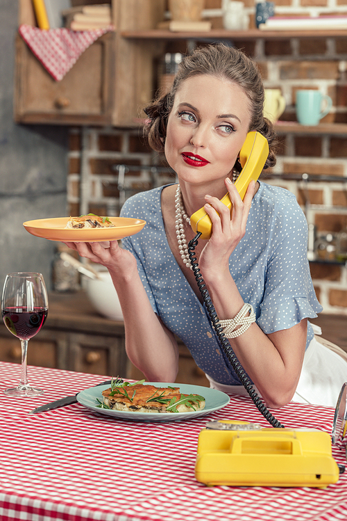 attractive adult housewife with freshly baked cake talking by vintage rotary phone at kitchen