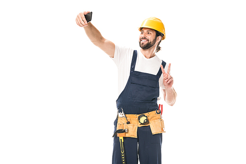 happy handsome workman in hard hat and tool belt taking selfie with smartphone isolated on white