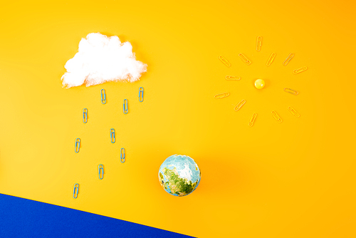 top view of environment composition with earth globe and cloud with sun made of paper clips on yellow