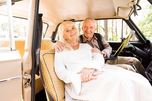 senior man hugging woman in beige car