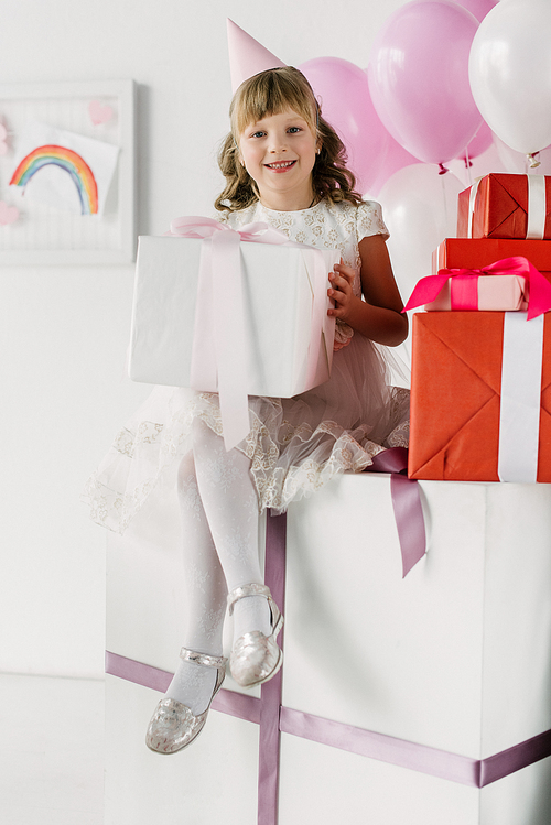 adorable birthday kid in cone sitting with gift boxes