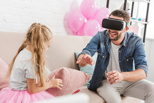 cheerful dad and daughter having fun and using virtual reality headset on sofa