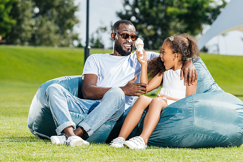 african american daughter having fun with ice cream while sitting on beanbag chairs with father