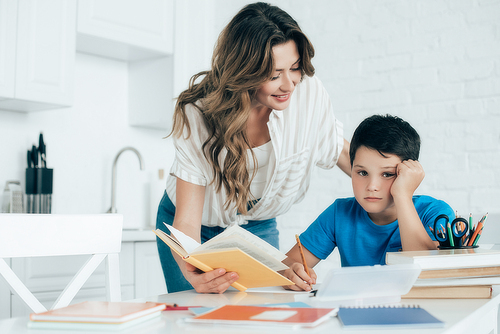 portrait of mother helping bored son with homework at home