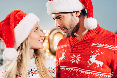 happy couple in santa hats looking at each other on christmas eve