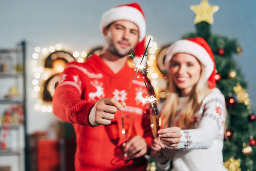 selective focus of couple in santa hats holding sparklers on christmas