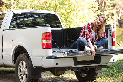 happy attractive woman sitting in trunk of pick up car outdoors