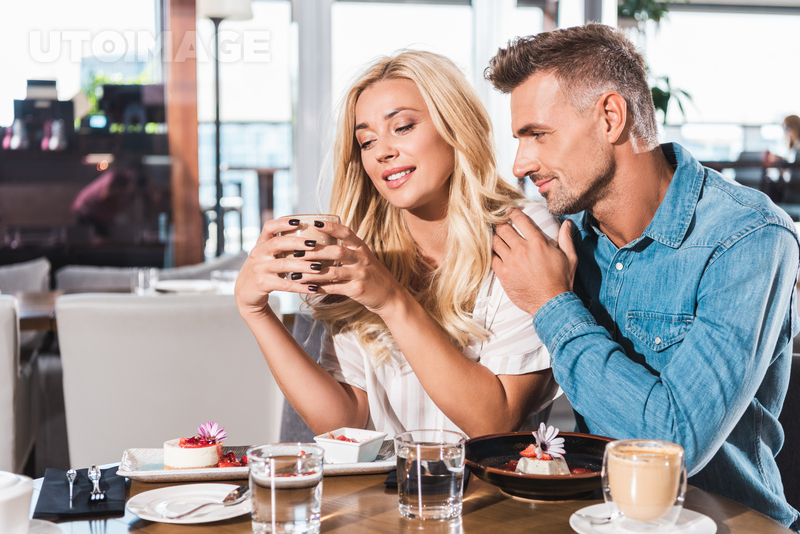 유토이미지 | boyfriend hugging cheerful girlfriend and she holding cup of coffee at table in cafe
