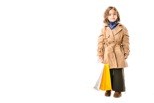 adorable stylish child in trench coat with colorful shopping bags  isolated on white