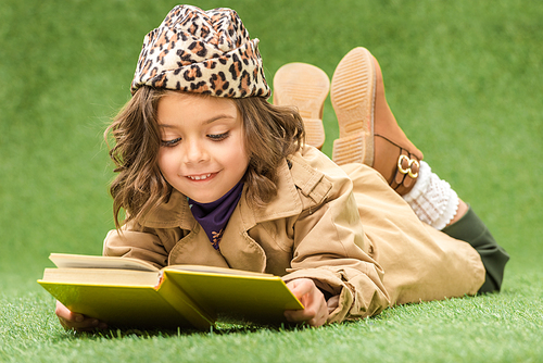 stylish kid reading book while lying on green grass