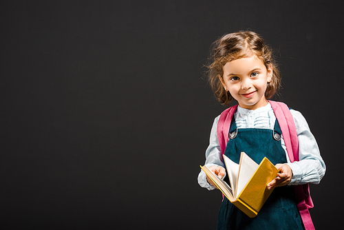 cute schoolgirl with backpack and book in hands  isolated on black