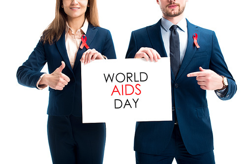 cropped image of businesspeople with red ribbons on suits pointing on card with world aids day text isolated on white