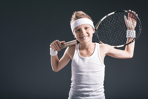 portrait of cheerful boy in sportswear with tennis racket on dark background