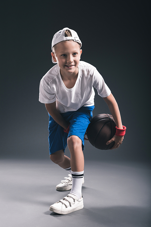 stylish boy playing basketball on grey background