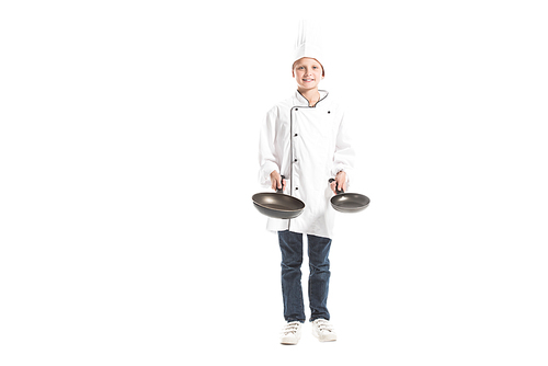 smiling boy in white chef uniform and hat holding frying pans and  isolated on white