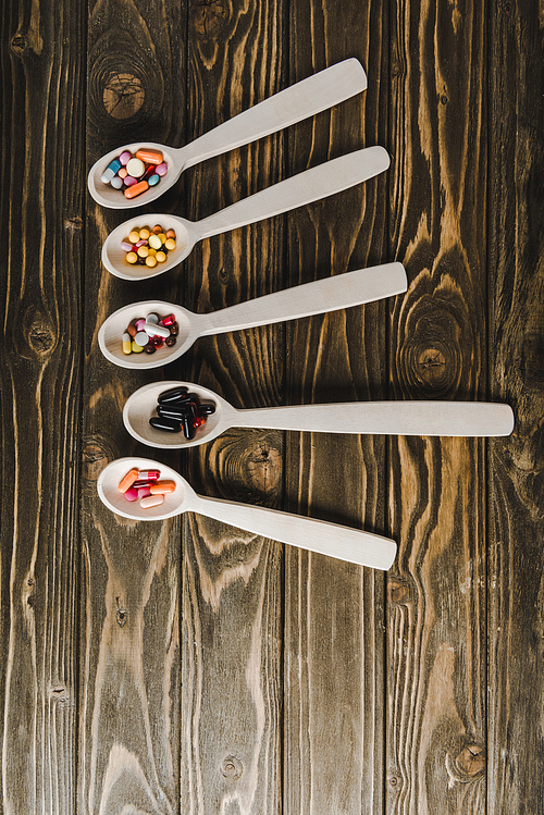 elevated view of spoons with colored pills on wooden tabletop