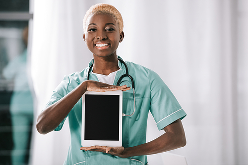 smiling african american nurse with stethoscope holding digital tablet with blank screen