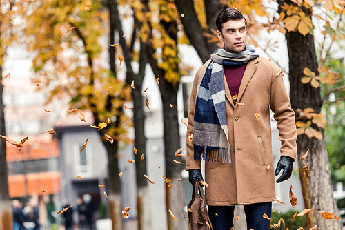 handsome stylish man in coat walking by autumnal street