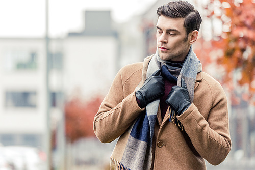 handsome man in coat, leather gloves and scarf standing on autumnal street