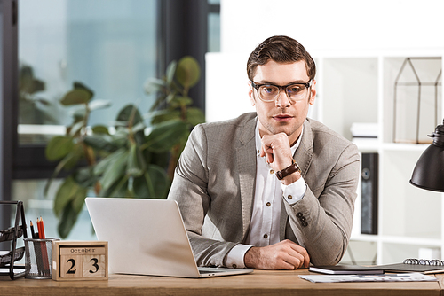 handsome confident businessman sitting at workplace and  in modern office