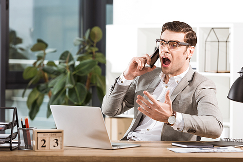 angry businessman talking by phone and screaming at workplace in office