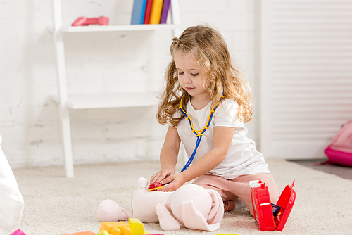 adorable child examining soft rabbit toy with stethoscope in children room