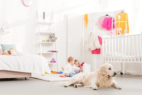 adorable sisters playing with toys, golden retriever lying on foreground in children room