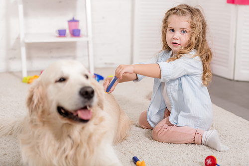 adorable preschooler pretending veterinarian and examining golden retriever in children room