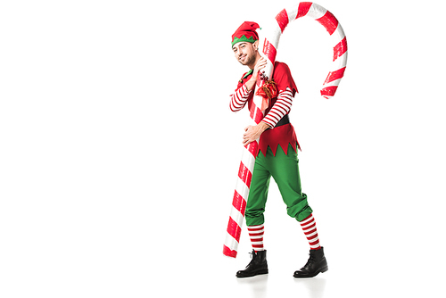 man in christmas elf costume carrying big candy cane isolated on white