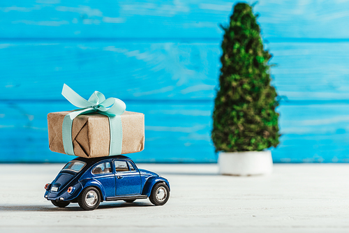 close-up shot of toy car with gift box and miniature christmas tree on blue wooden background