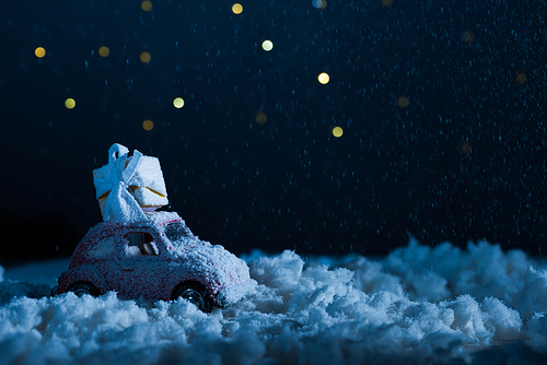 close-up shot of toy car with gift box standing in snow in night, christmas concept