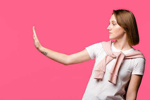 side view of young woman showing stop gesture isolated on pink