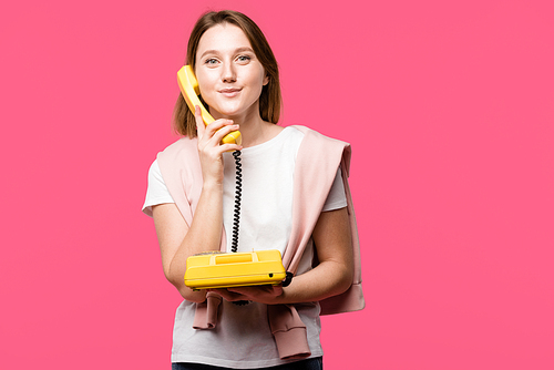 beautiful young woman talking by rotary phone and smiling at camera isolated on pink