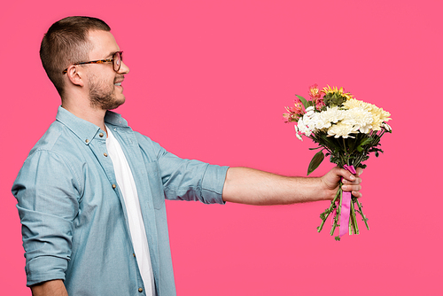 side view of happy young man holding bouquet of flowers isolated on pink