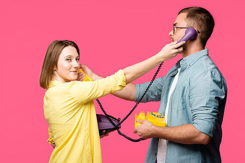 young man and woman holding rotary phones and handsets for each other isolated on pink