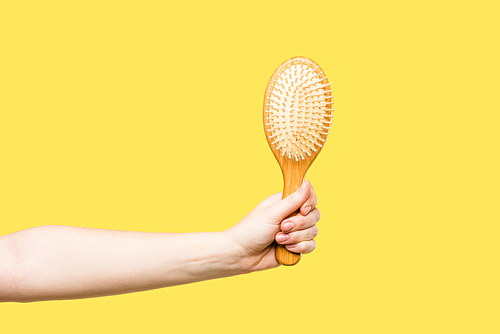 cropped shot of person holding hairbrush isolated on yellow