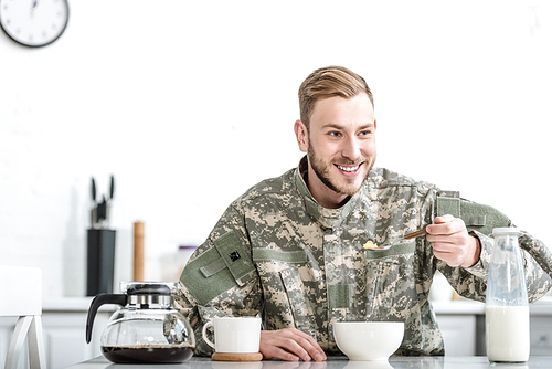 Smiling man in military uniform eating cornflakes at kitchen