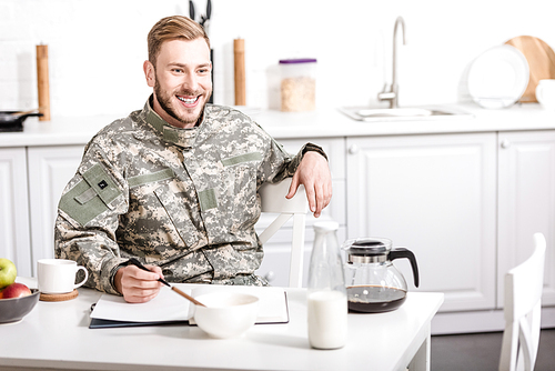 smiling army soldier sitting at kitchen table and having breakfast