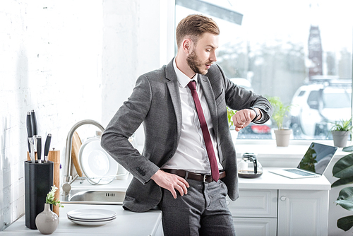 successful handsome businessman looking at watch in kitchen