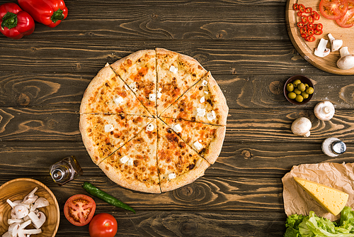 top view of cheese pizza with ingredients and vegetables on wooden table